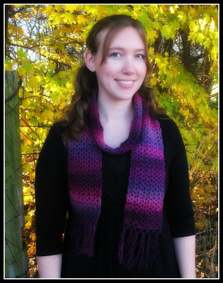 author wearing a pink and purple one skein crochet scarf in front of fall foliage