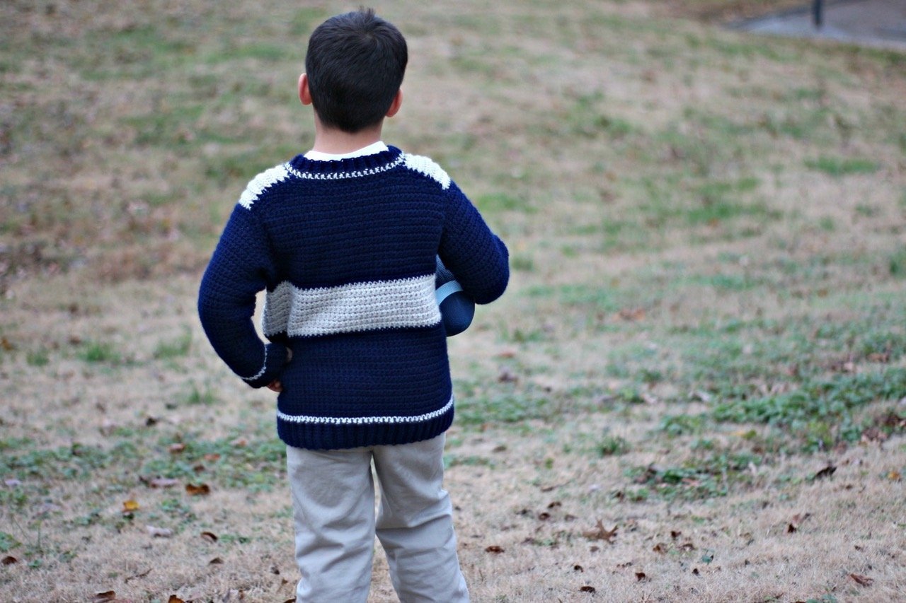 boy wearing a crochet boys sweater standing with his back to camera