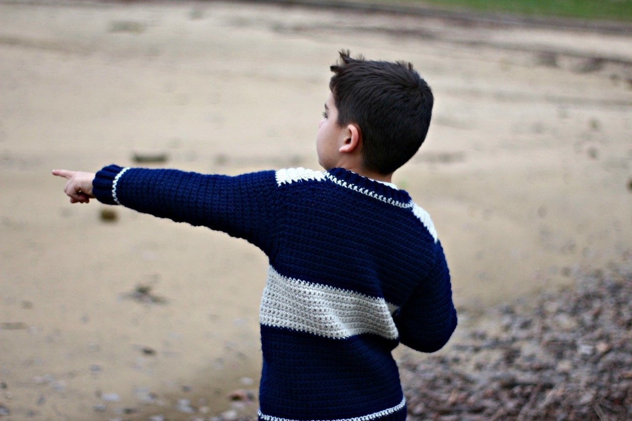 Young boy wearing crocheted sweater pointing off in distance
