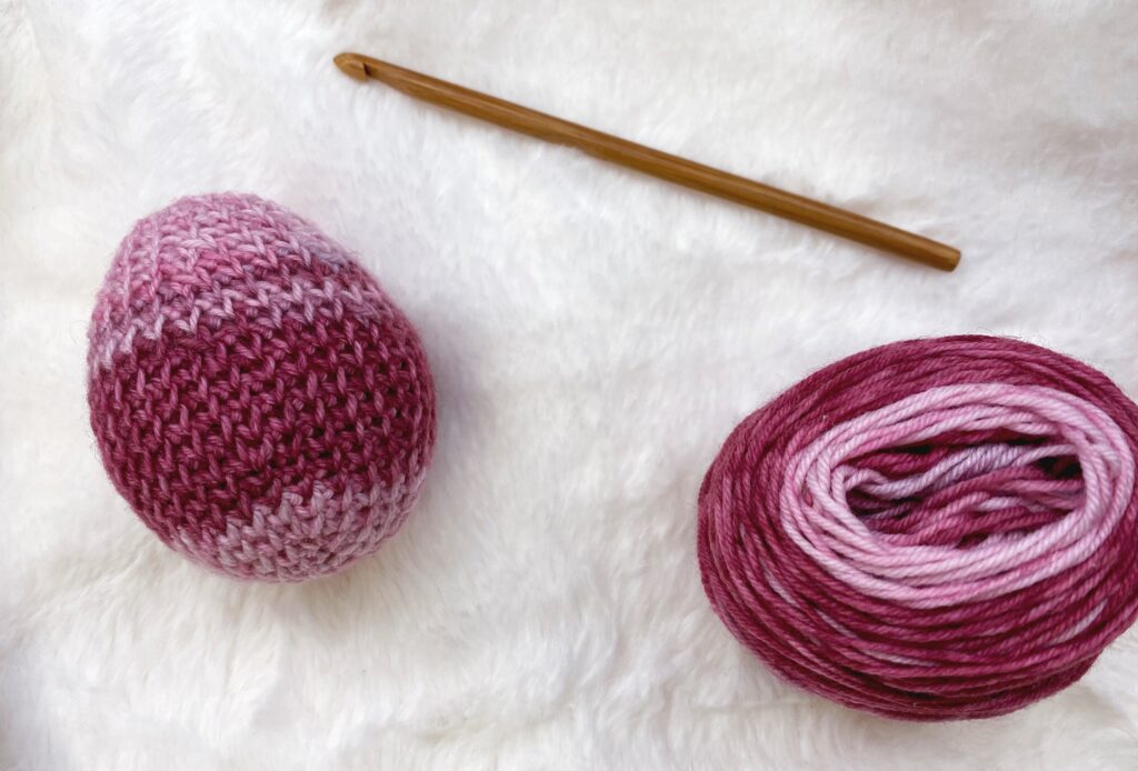 crochet Easter egg next to yarn and hook on white fur background