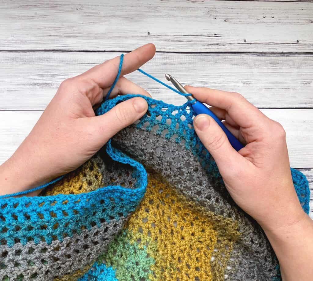in progress photo of hands holding crochet hook and working on crochet triangle shawl
