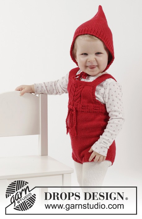 toddler wearing red romper and bonnet standing next to chair