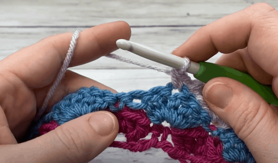 a hand doing Sc in center double crochet stitch of next shell